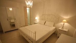 Quarto com uma cama de casal, duas mesas de cabeceira com luminárias, um candelabro, um guarda-roupa e um espelho.