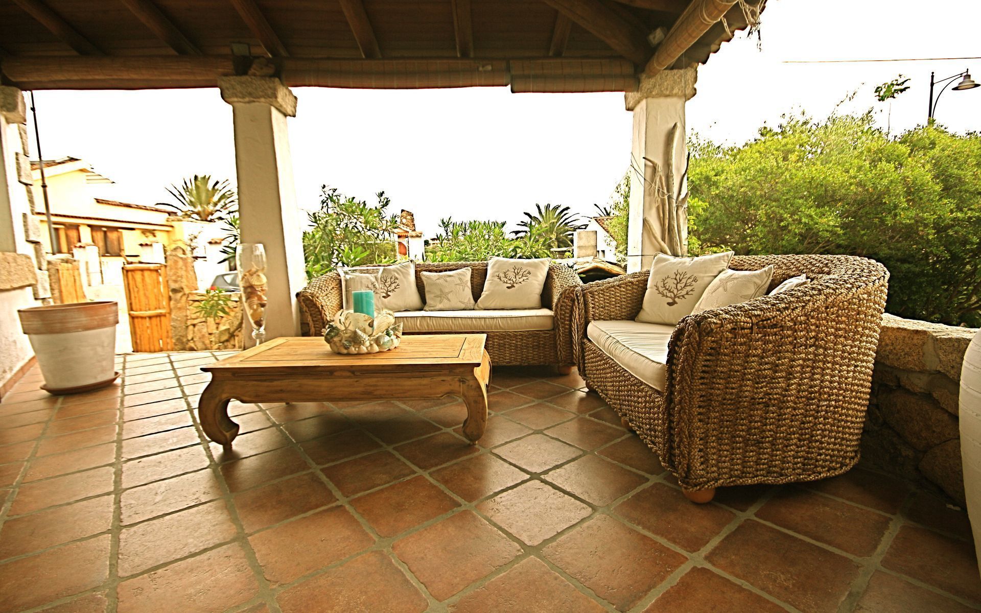 An outdoor patio with wicker furniture, a tiled floor, and potted plants.