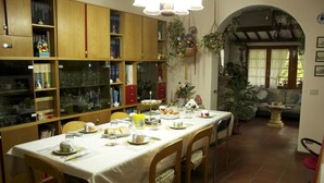 A dining area with a table set for a meal, surrounded by wooden cabinets and shelves filled with books and glassware. - B&B Il Prato (Predappio)