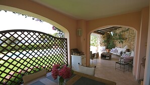 Un interior acogedor con una zona de estar, una mesa con un jarrón de flores y vistas a un espacio exterior a través de una puerta celosía.