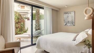 A bedroom with a bed, a chair, a sliding glass door to a balcony, and a painting on the wall.