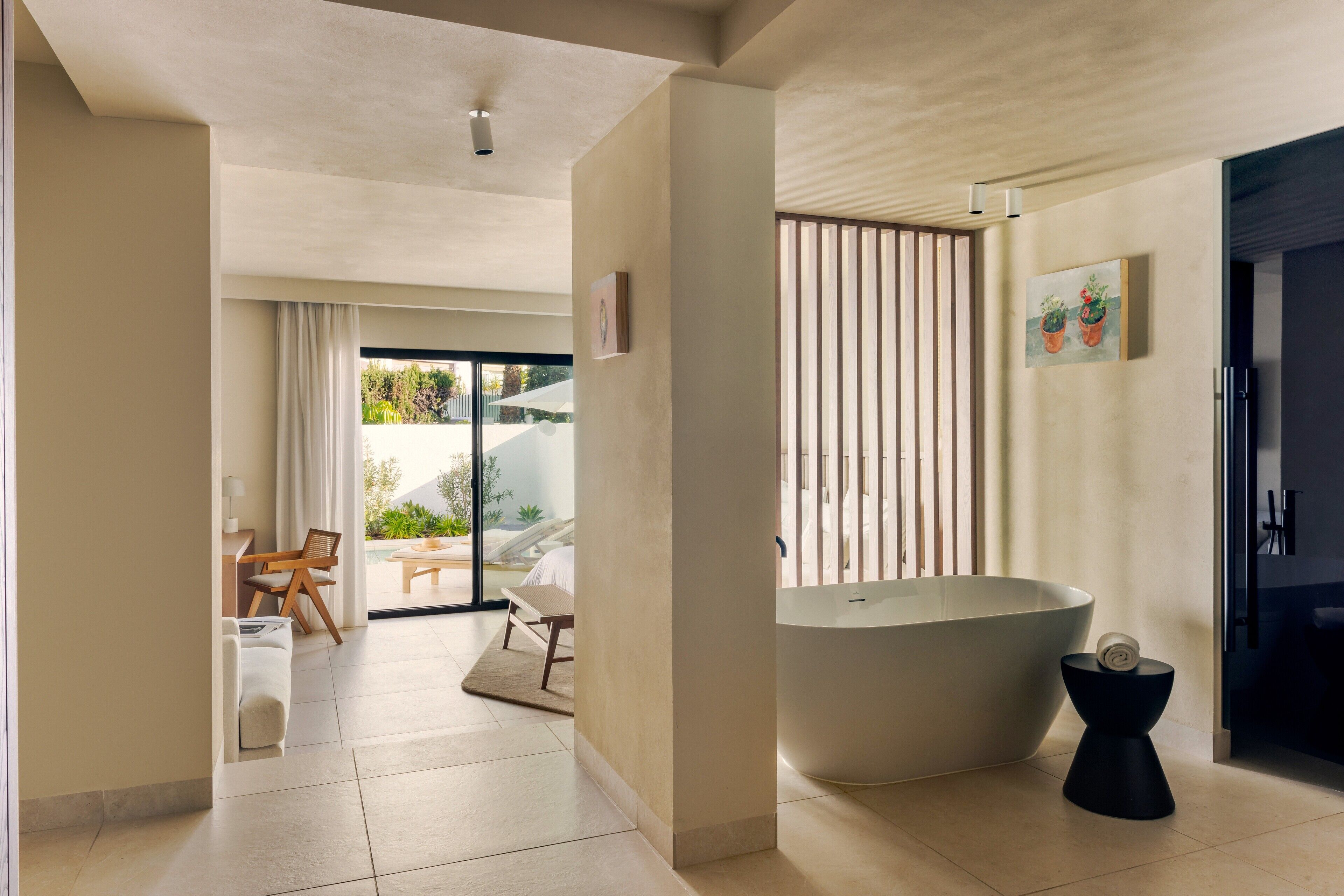 A modern hotel room with a large bathtub, a dining area with a table and chairs, and a view of the outdoors.
