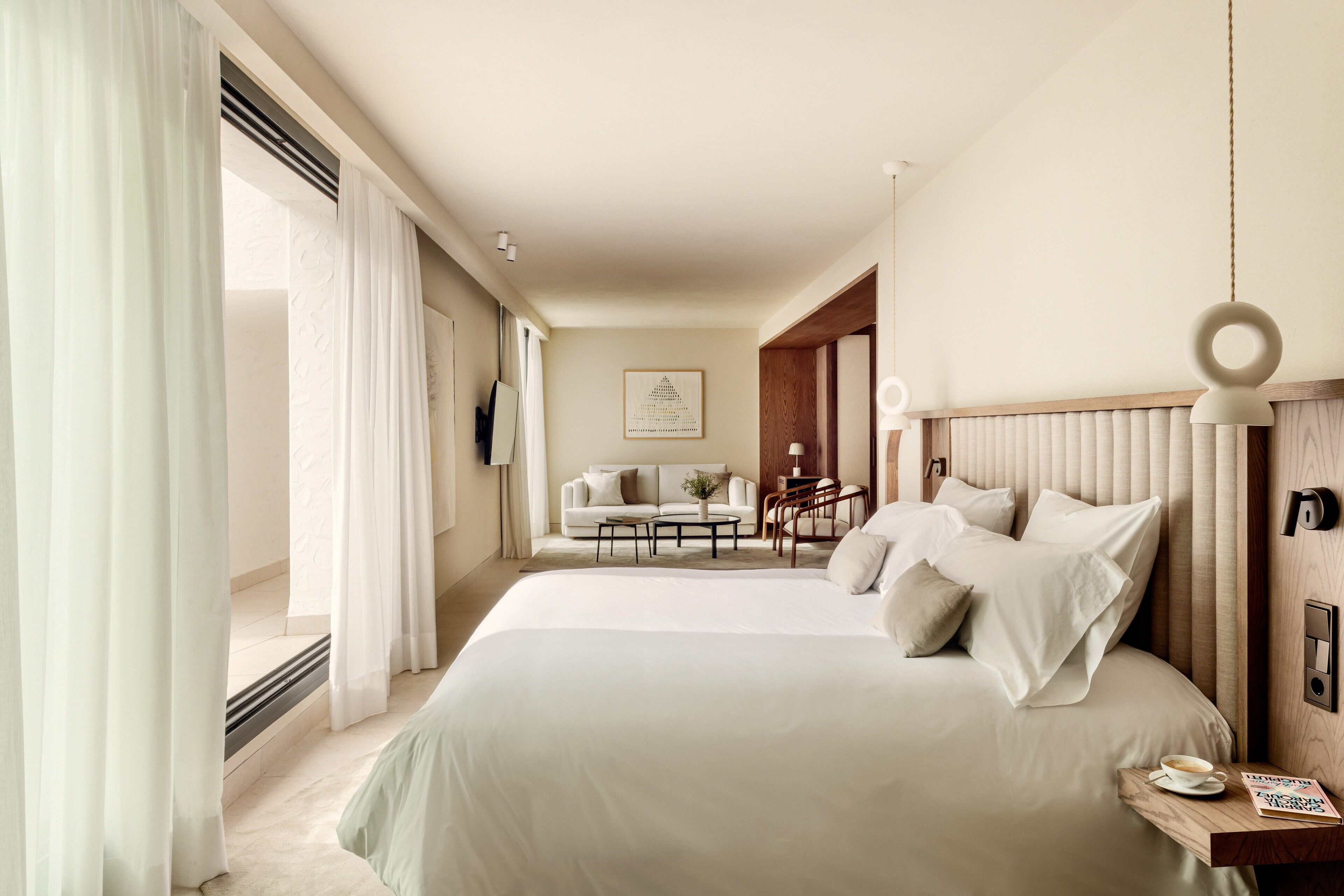 A hotel room with a large bed, a sofa, a coffee table, and a desk with a lamp.