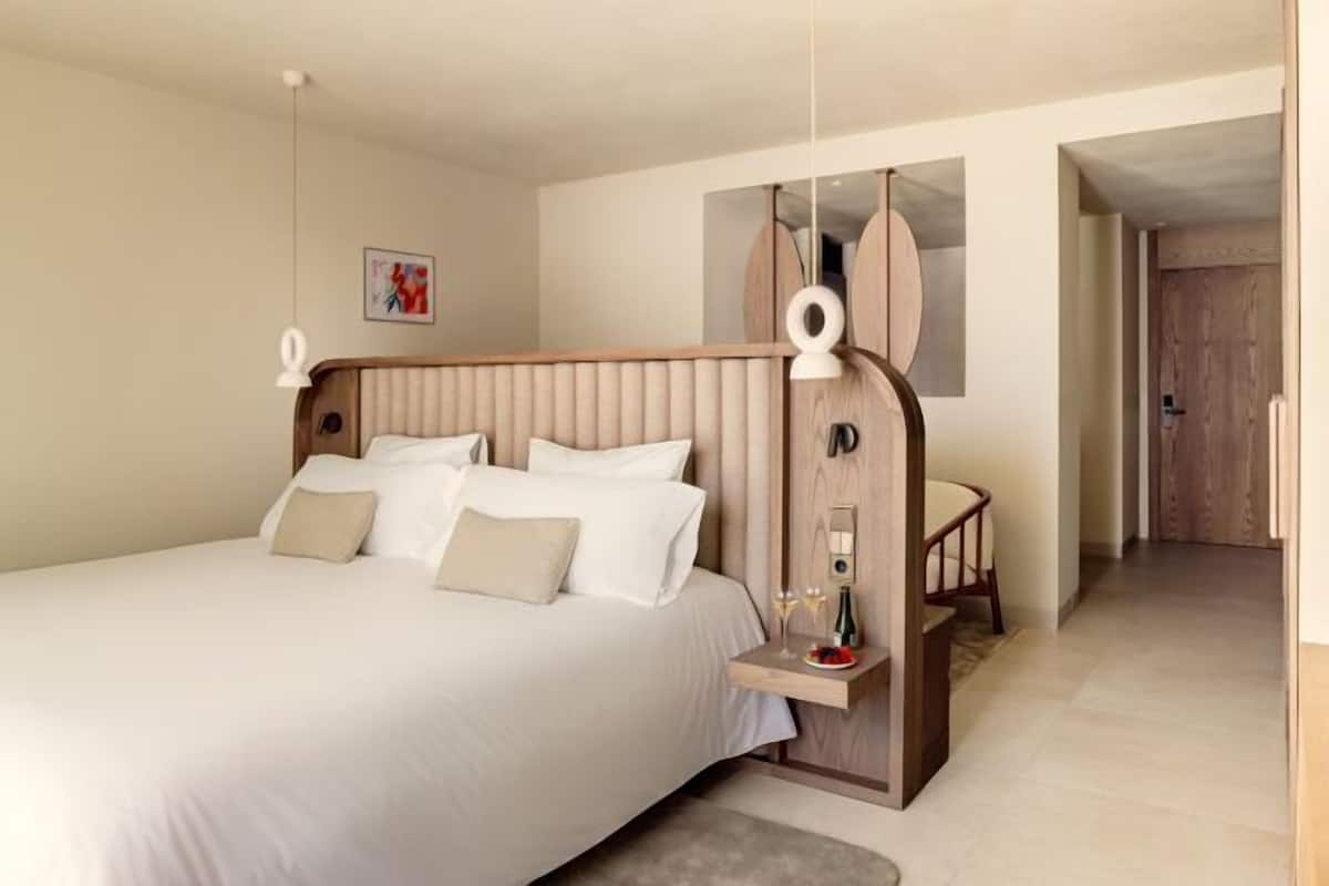 A modern hotel room with a large bed, bedside table, and a small seating area.