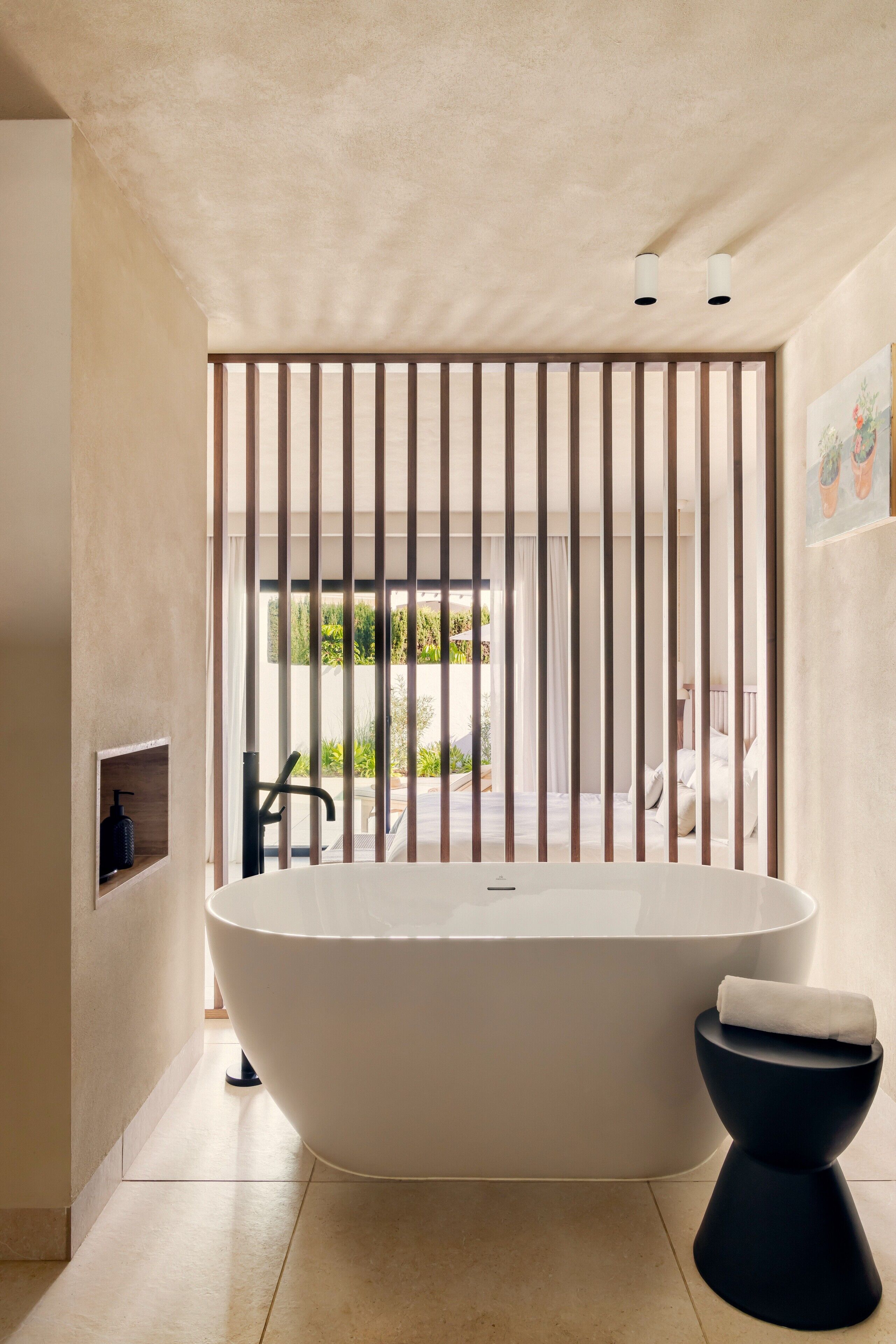 Een moderne badkamer met een vrijstaand bad, een zwart zuilwastafeltje en uitzicht op het groen door een groot raam.