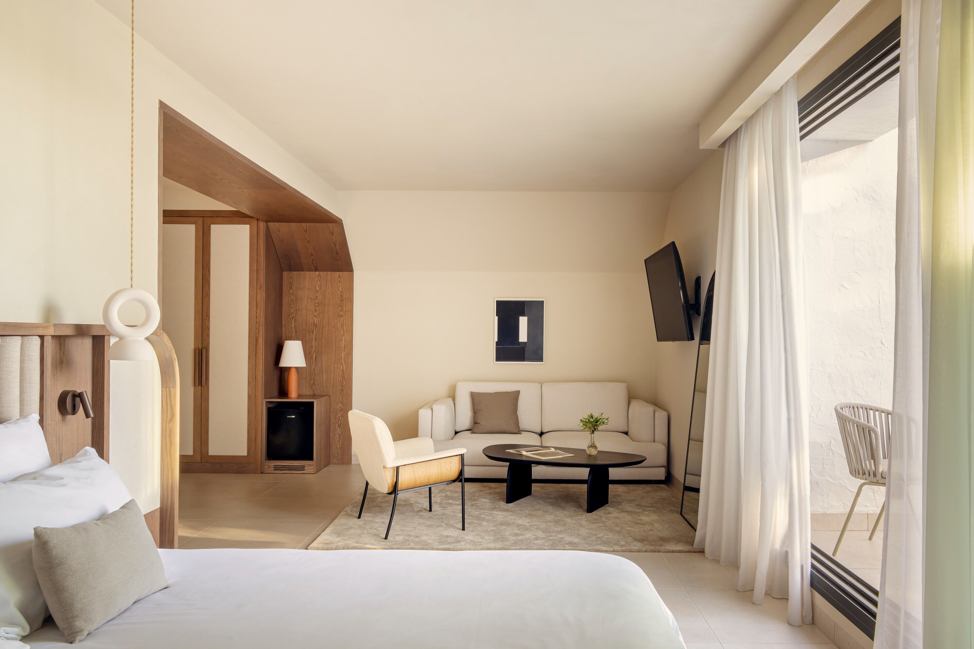 Une chambre d’hôtel moderne équipée d’un lit, d’un canapé, d’une table basse, d’une télévision et d’une grande fenêtre avec des rideaux.