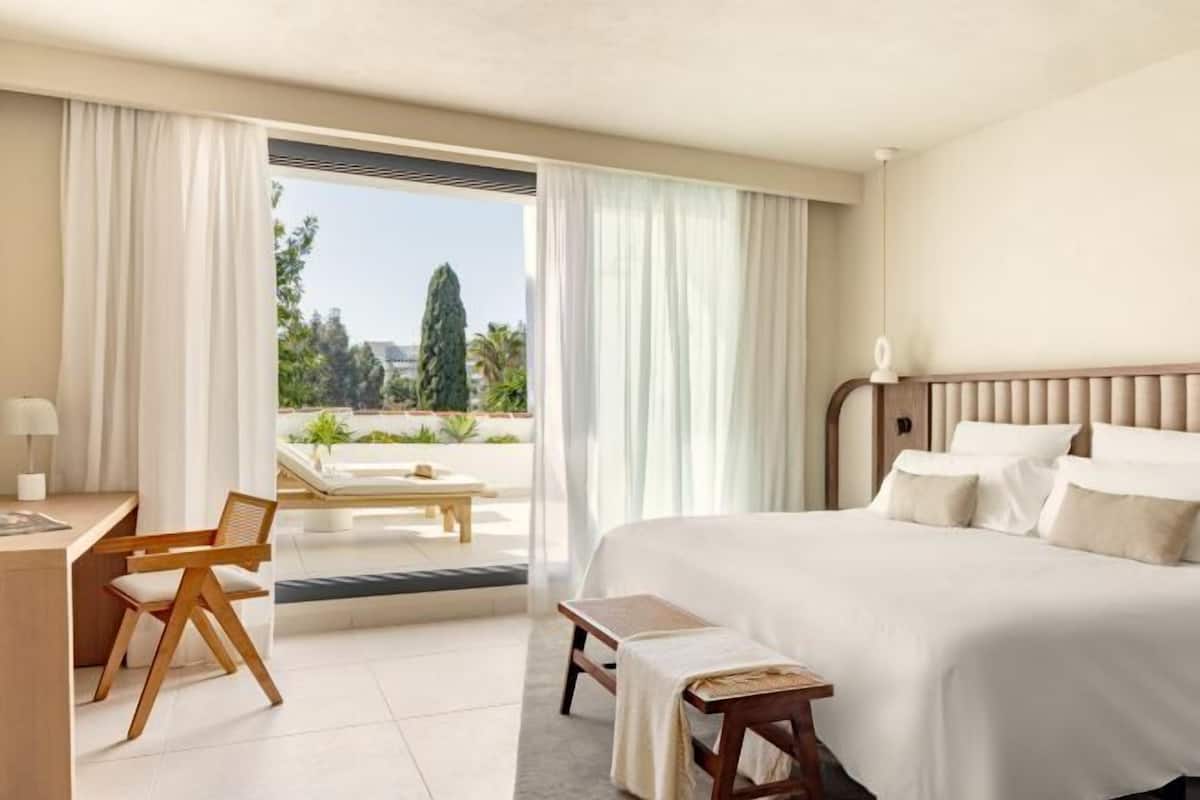 A hotel room with a bed, a desk, a chair, and a view of the outdoors.
