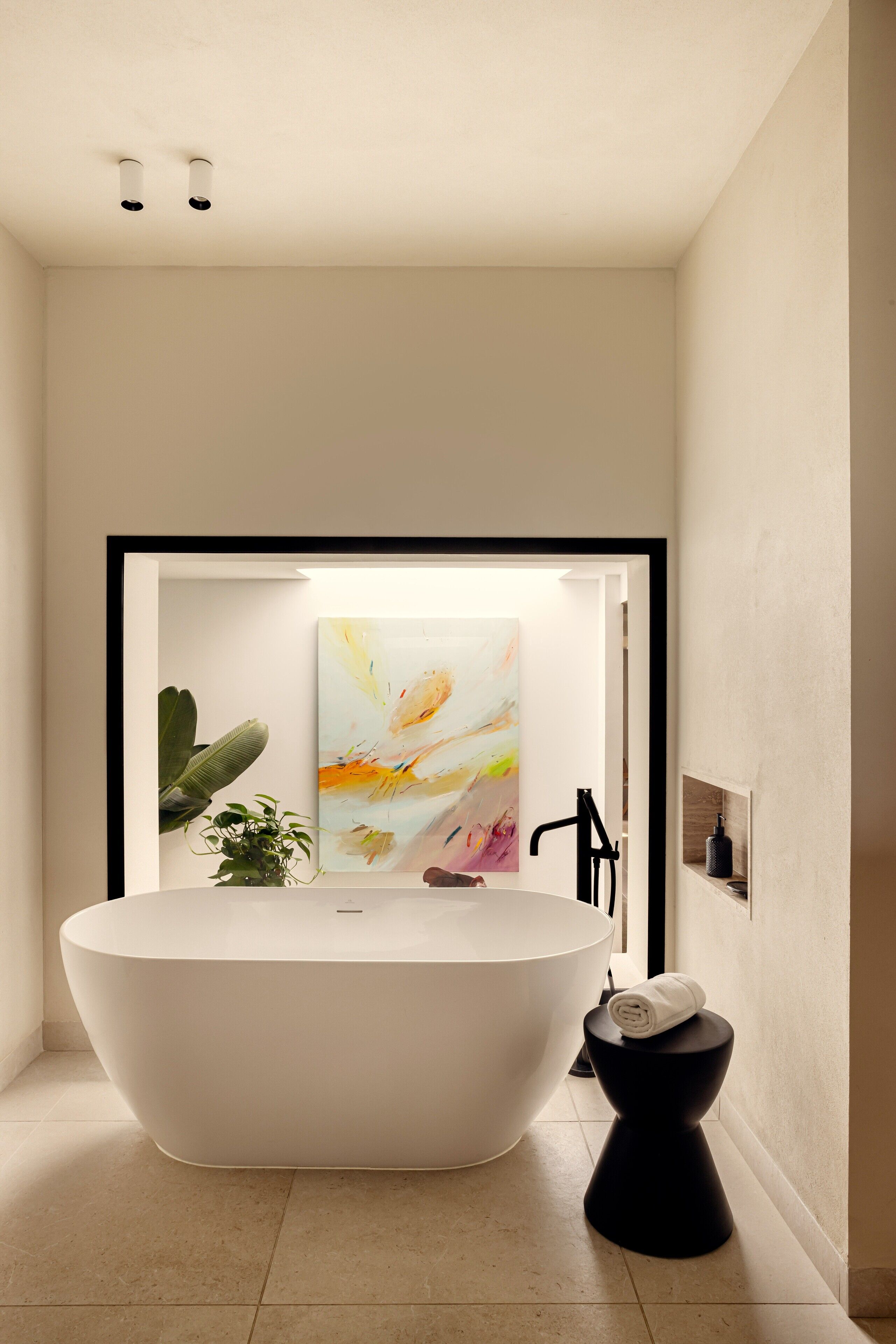 Un baño moderno con una bañera independiente, un inodoro negro y un lavamanos instalado en la pared.