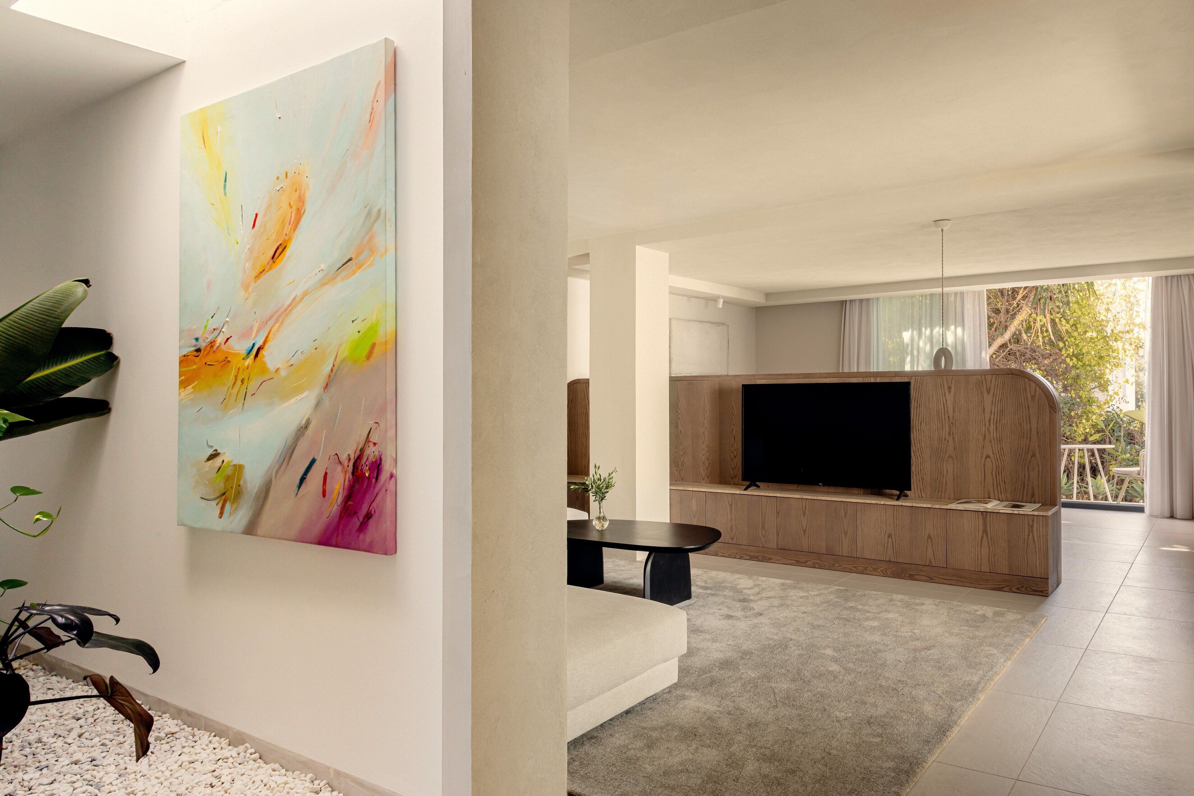 A modern living room with a large abstract painting, a flat-screen TV, and a wooden entertainment unit.