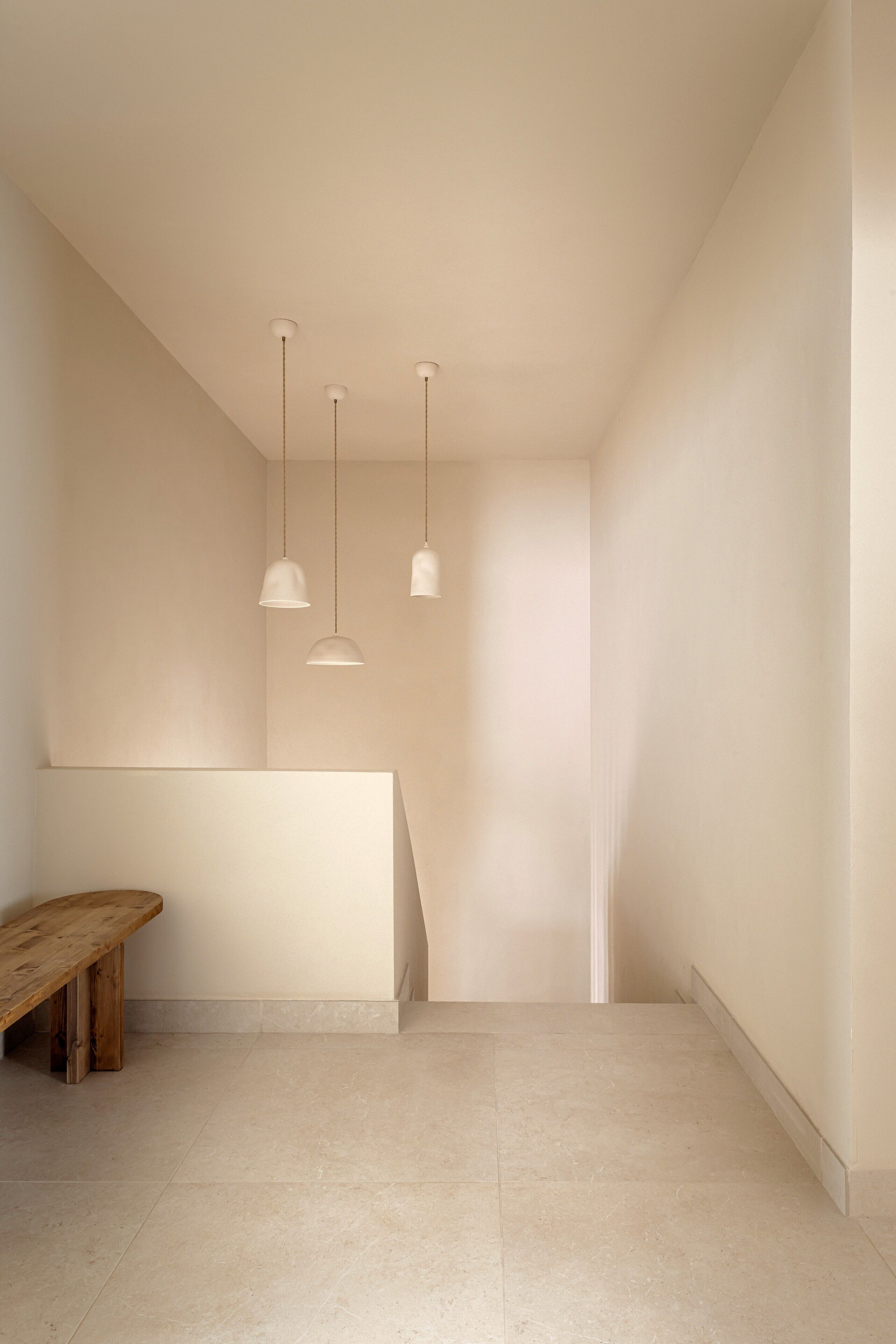 A minimalist room with a wooden bench, a white reception desk, and three pendant lights.