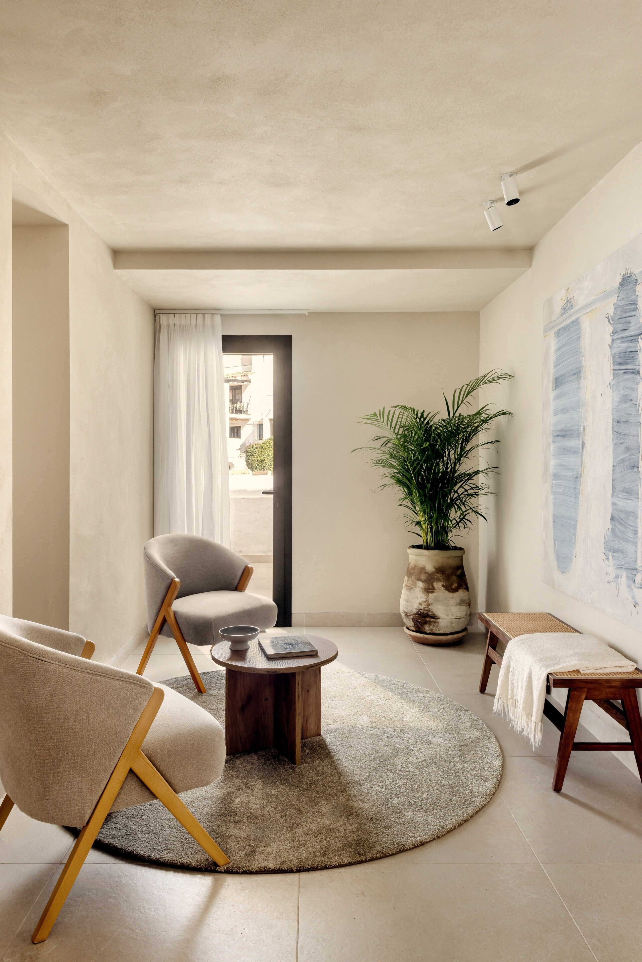 A modern living room with a round rug, a coffee table, a chair, a potted plant, and a painting on the wall.
