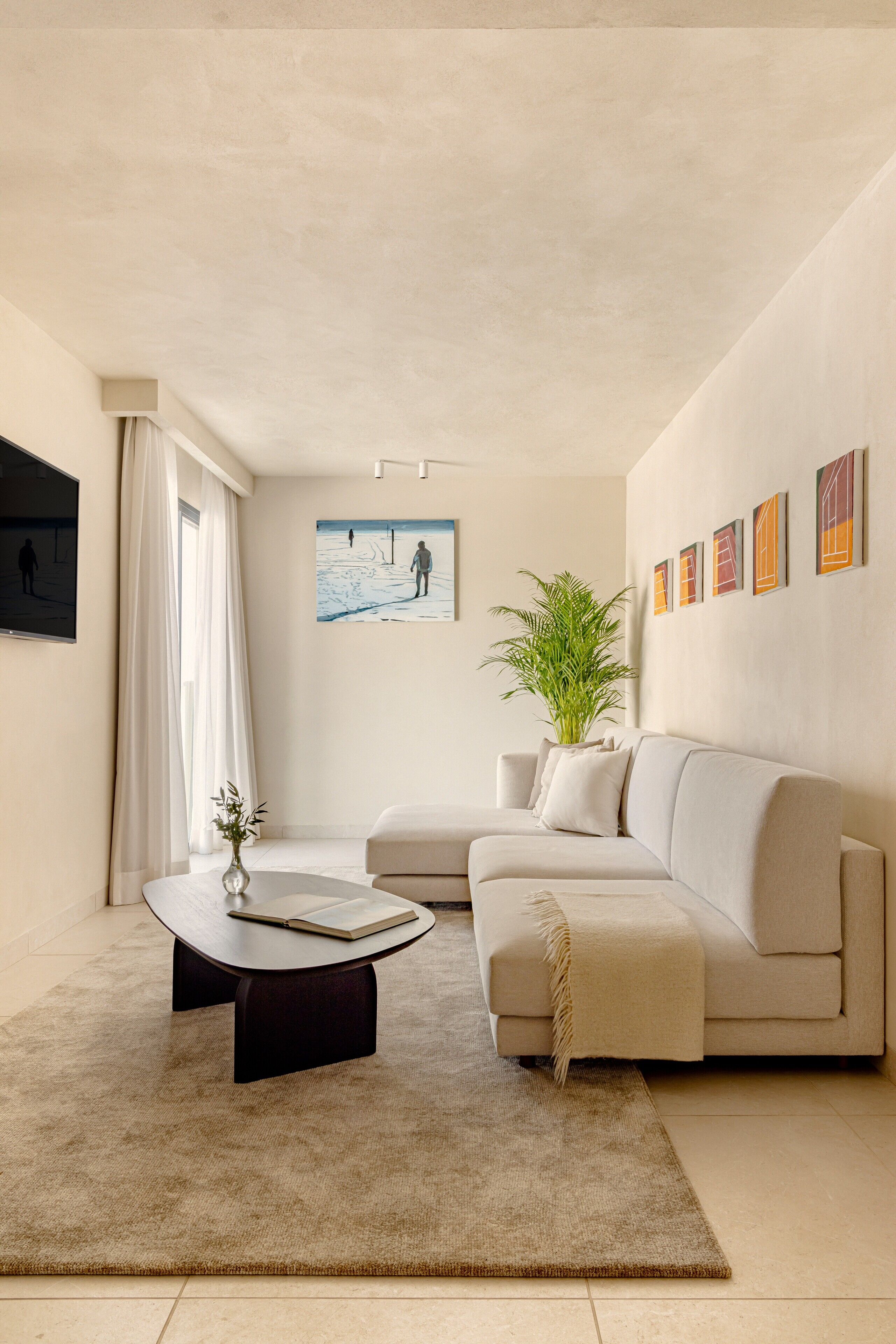 Un salon moderne avec un canapé beige, une table basse, une plante en pot et des œuvres d’art accrochées au mur.
