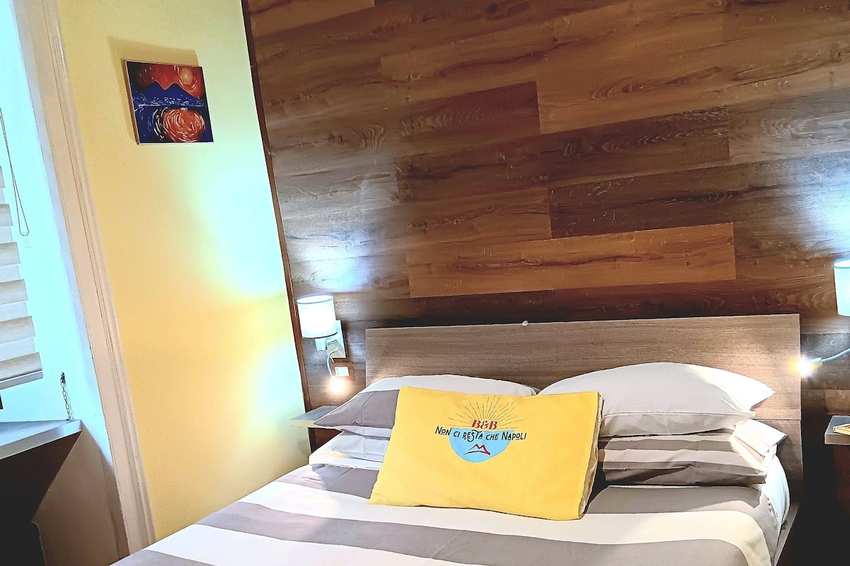 A hotel room with a wooden headboard, a bed with striped bedding, and a yellow pillow with text.