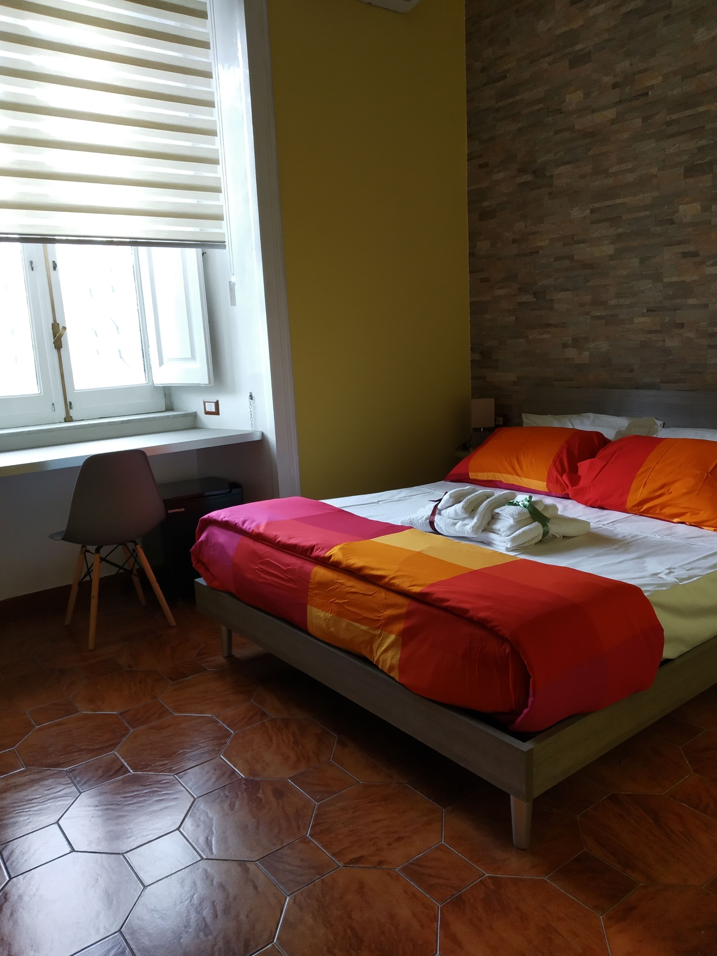 A bedroom with a bed, a chair, a window, and a brick wall.