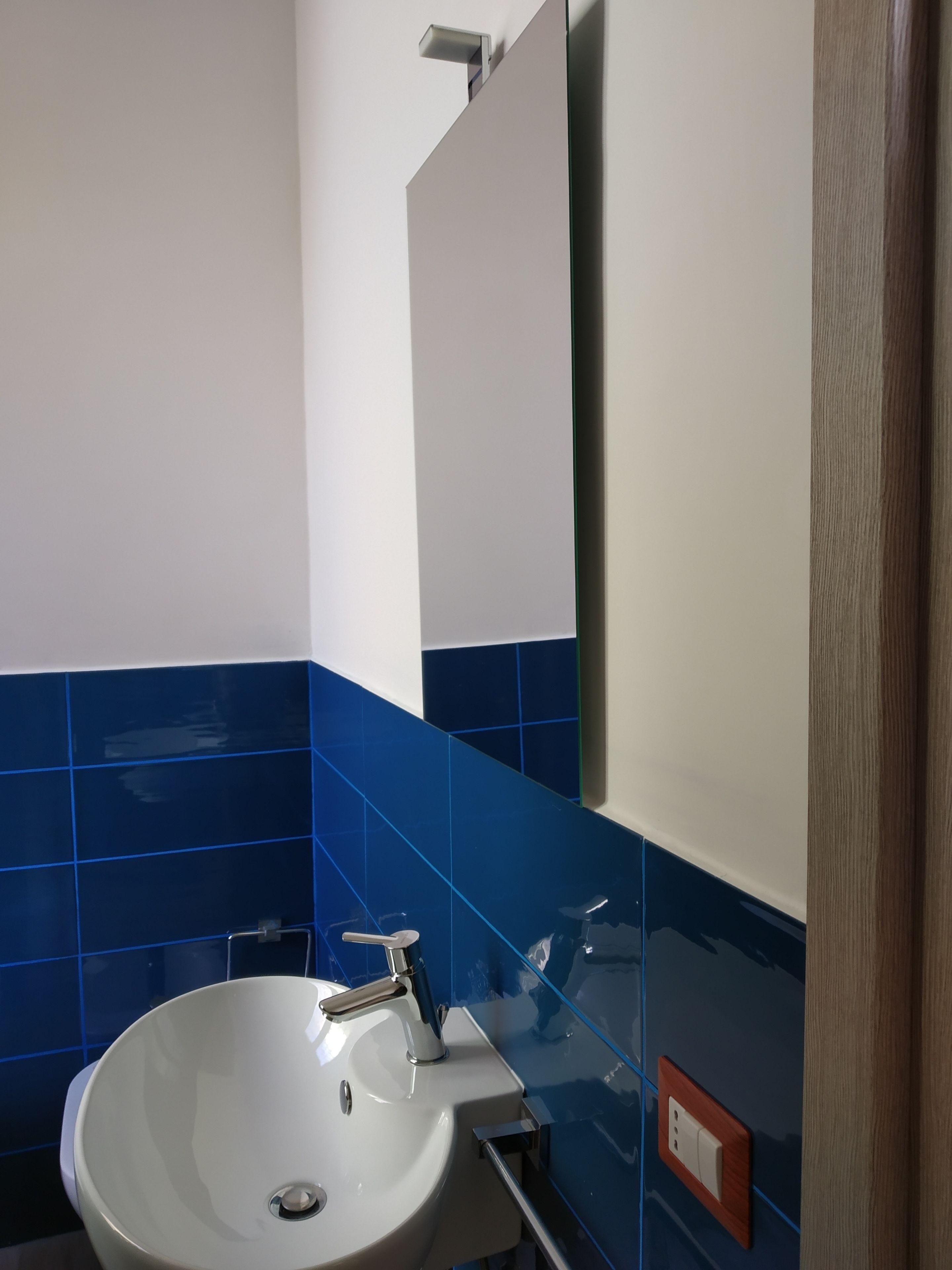A bathroom with a white sink, blue tiles, a mirror, and a wooden door.