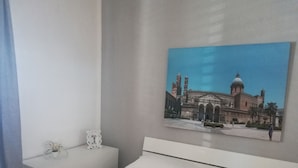 A bedroom with a bed, a nightstand, and a wall-mounted painting of a building. - B&B Il Poeta (Palermo)