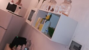 A compact kitchen with a microwave, a small refrigerator, and a shelf with jars and a vase. - B&B Il Poeta (Palermo)