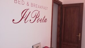 A room with a wall sign reading "BED & BREAKFAST" and "El Poeta". There is a clock on the wall, a door, and a small table with various items including a framed picture, a book, and a decorative object. - B&B Il Poeta (Palermo)