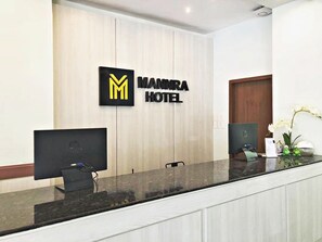 A reception desk at the MAMMARA HOTEL with a logo, a computer monitor, and a small plant. - Mannra Hotel (Manila)