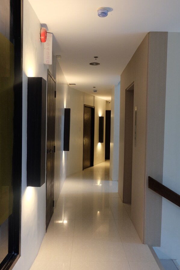A modern hotel corridor with a shiny tiled floor, dark wooden doors, and recessed lighting. - Mannra Hotel (Manila)