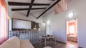 Una sala de estar con sofá, una mesa de comedor con sillas, una zona de cocina con armarios y estufa, y un dormitorio con cama y cortinas.