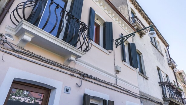 Un edificio de fachada rosa claro, con contraventanas negras y balcones de hierro forjado decorativos.