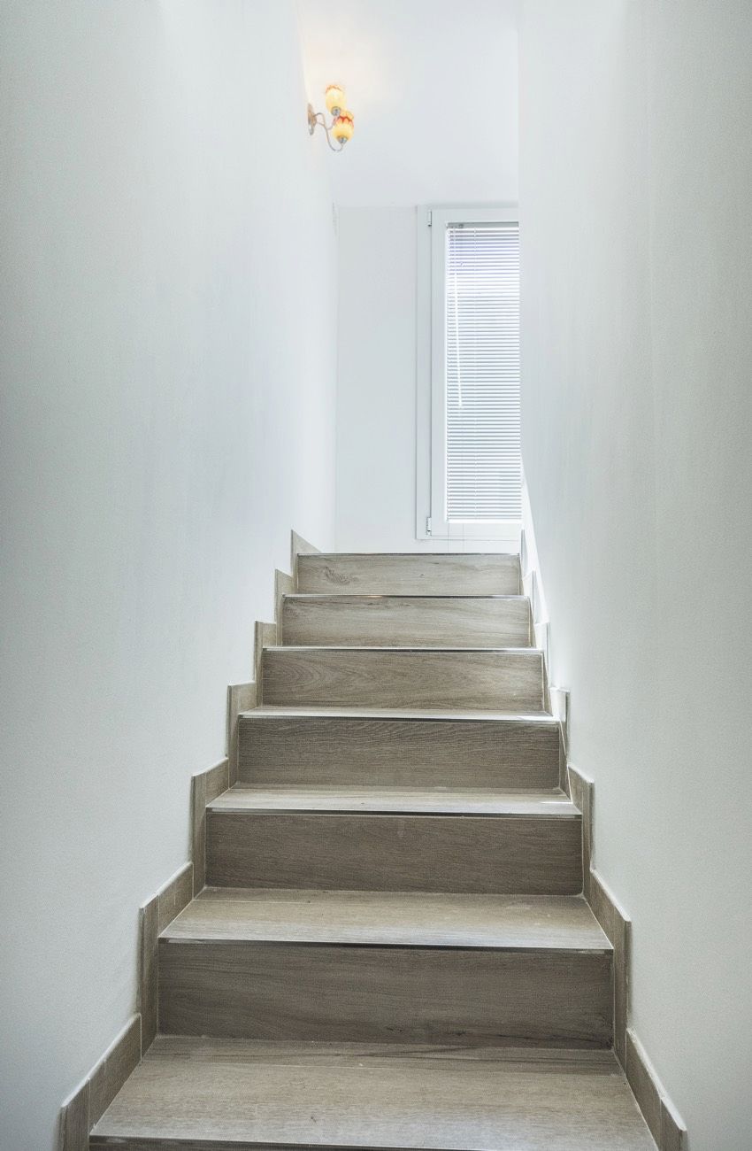 Un escalier avec des marches en bois menant à une pièce dotée d’une fenêtre et d’un luminaire fixé au mur.