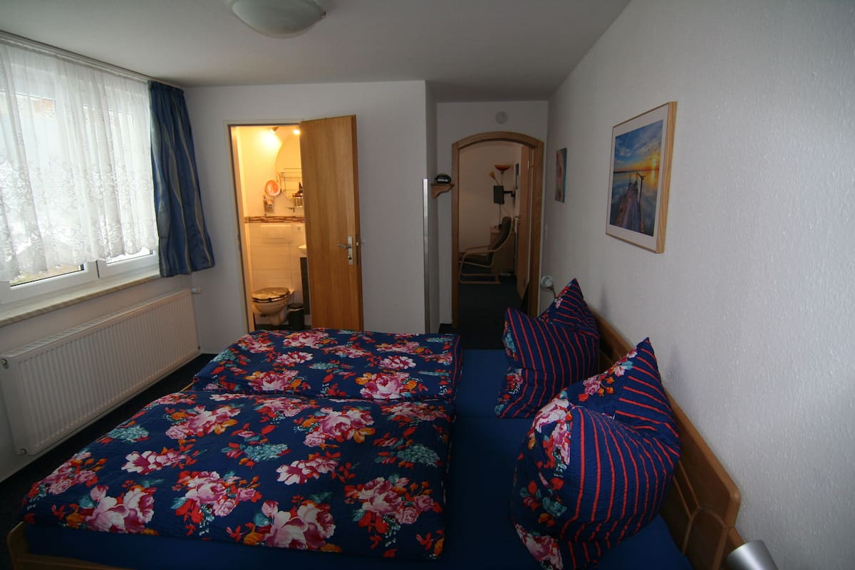 A bedroom with a floral bedspread, a wooden headboard, and a view of a bathroom through an open door.