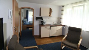 Una habitación de hotel compacta con kitchenette, una cama individual, una silla y una mesita.
