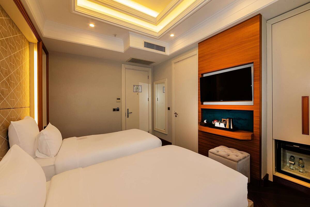 Ein Hotelzimmer mit zwei Betten, einem Fernseher, einer Minibar und einer Tür zu einem weiteren Raum.
