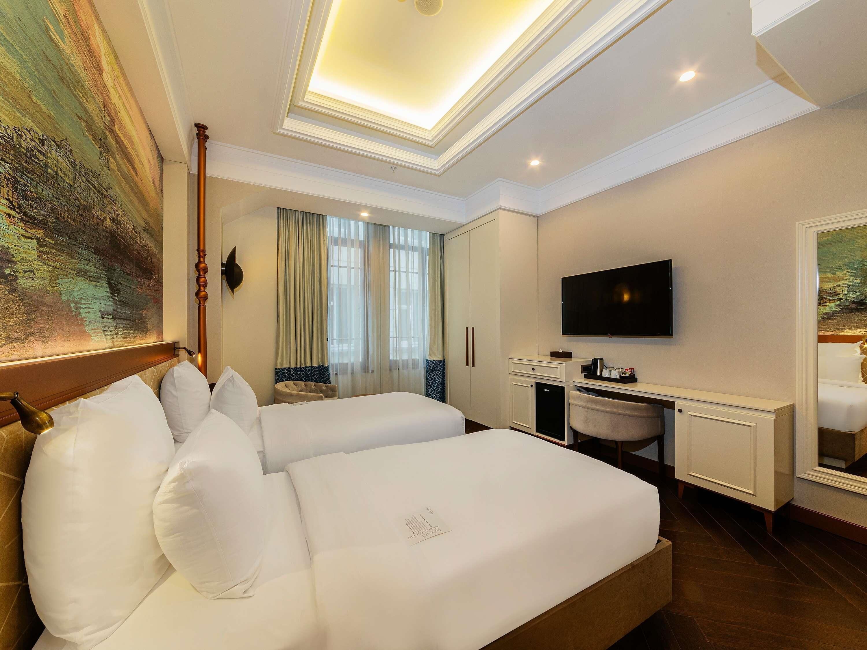 A hotel room with a bed, a desk, a television, and a large painting on the wall.