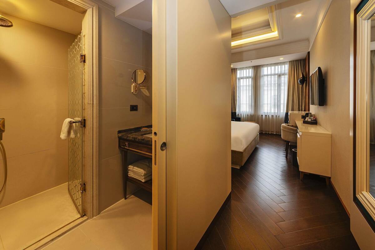 A hotel room with a shower, a bed, a desk, and a TV.