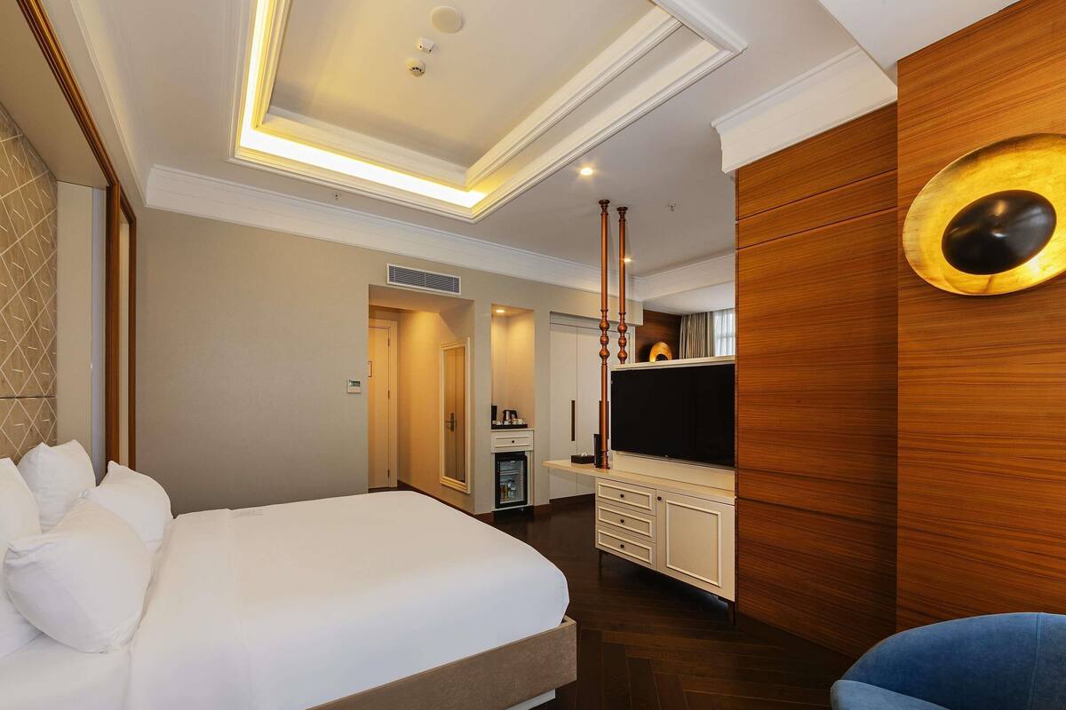A hotel room with a large bed, a TV, a minibar, and a wooden accent wall.