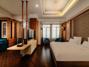 Une chambre dâhĂŽtel avec un grand lit, une tĂ©lĂ©vision, un bureau avec des tiroirs, deux chaises et une fenĂȘtre avec des rideaux.
