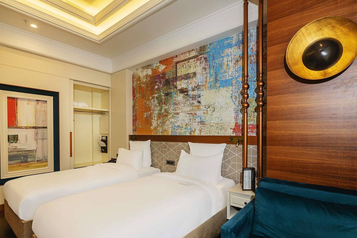 A hotel room with two beds, a large abstract painting, and a wooden accent wall.