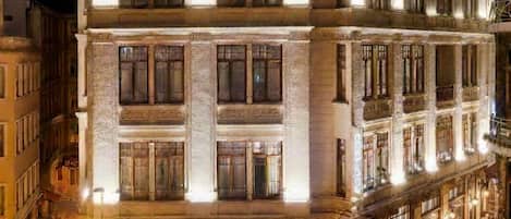 Un edificio de varios pisos con arquitectura clásica, que destaca por sus amplios ventanales y una entrada imponente con toldo.