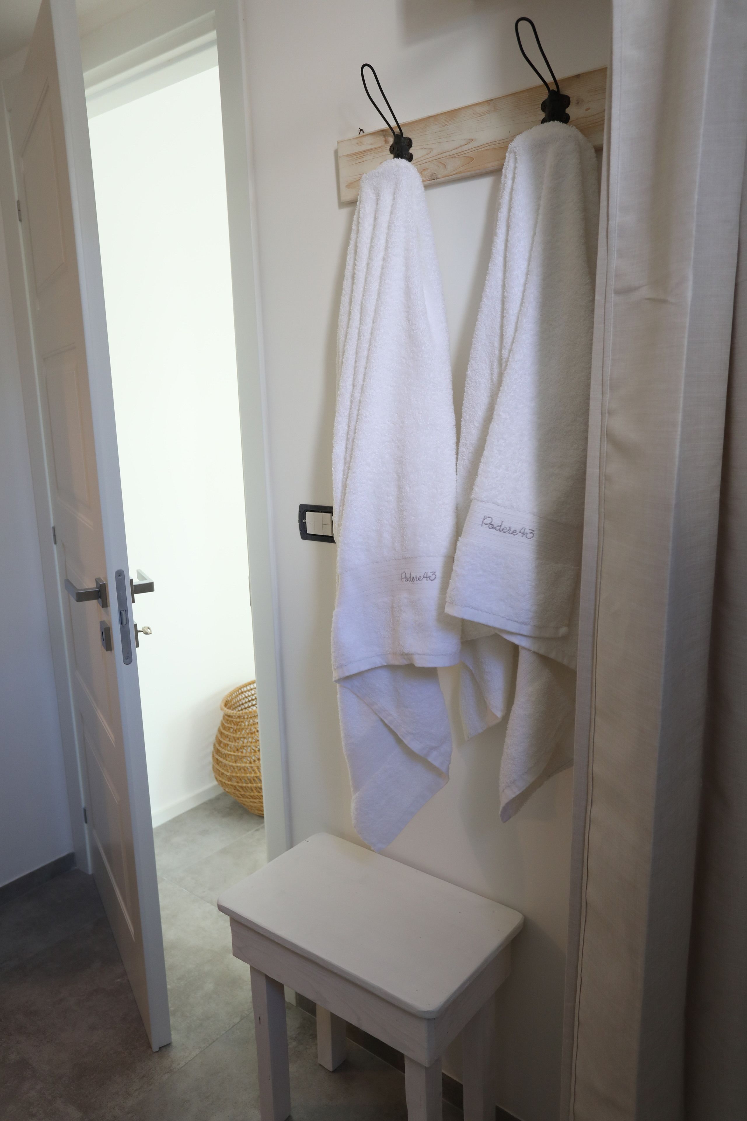 A bathroom with a white bench, a wooden towel rack, and a basket on the floor.