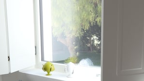 A bedroom with a window, a bed with grey and white pillows, and a green decorative item on the windowsill.