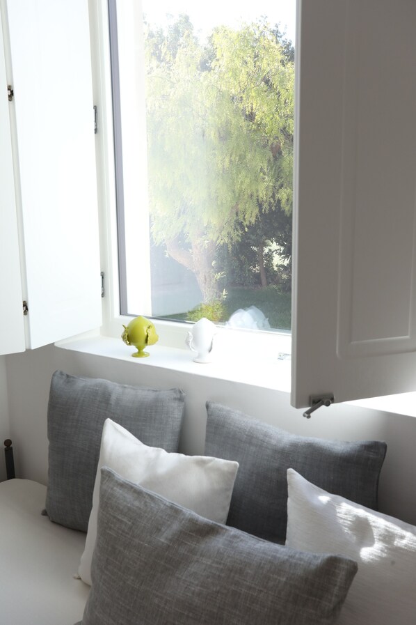 A bedroom with a window, a bed with grey and white pillows, and a green decorative item on the windowsill. - Podere 43 (Otranto)