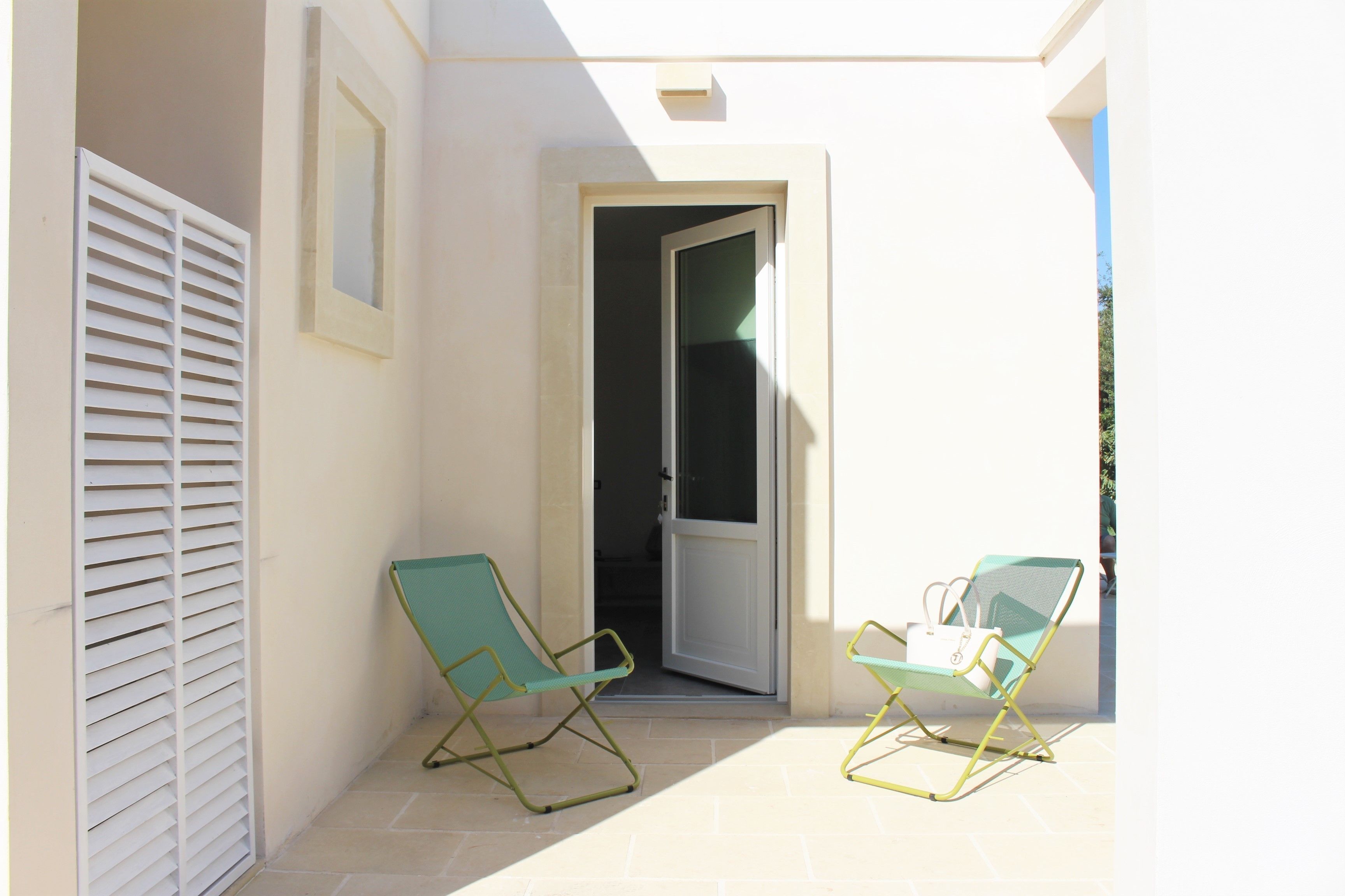 A small outdoor area with two green folding chairs and a white door leading to an interior space.
