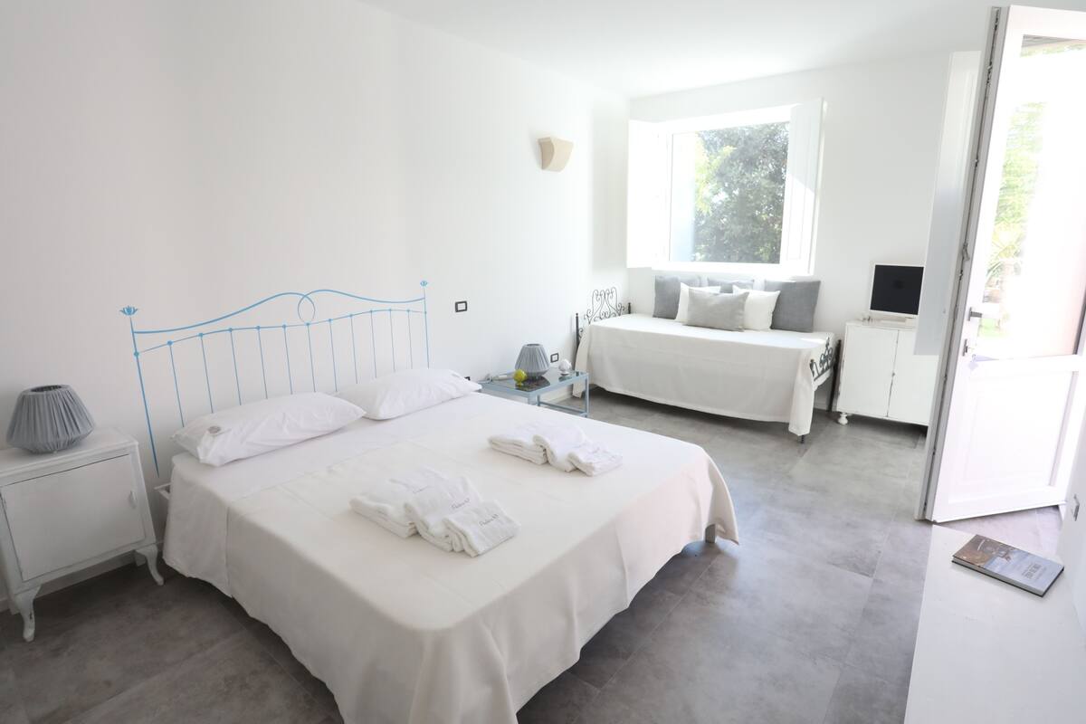 A bedroom with a large bed, bedside tables, a desk, and a window.