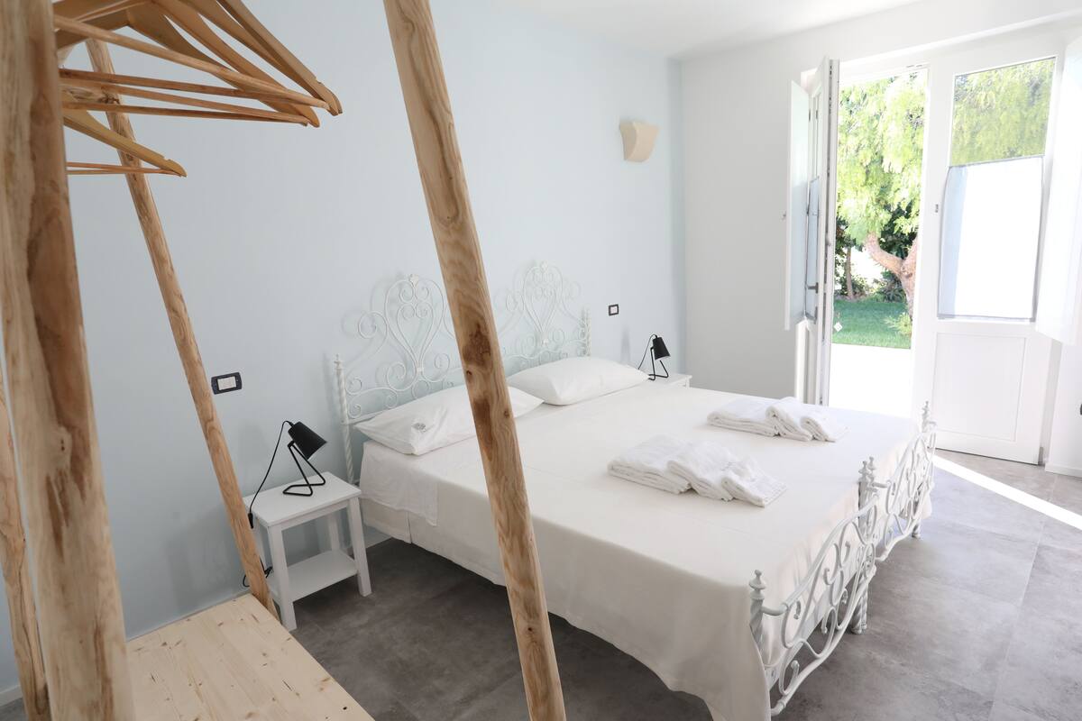 A bedroom with a large bed, bedside tables, and a view of the outdoors.