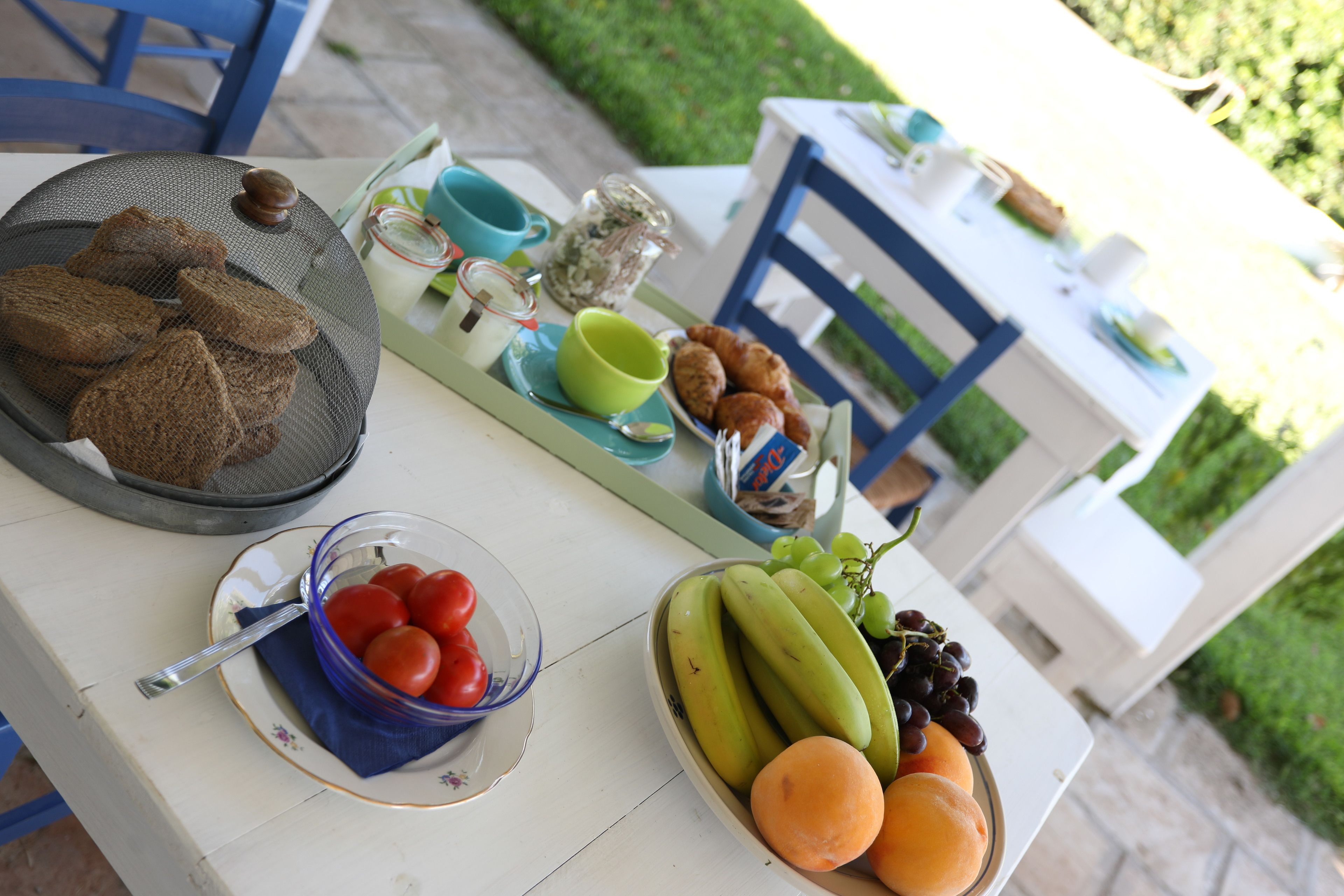 A table with food items including bread, tomatoes, bananas, grapes, and pastries.