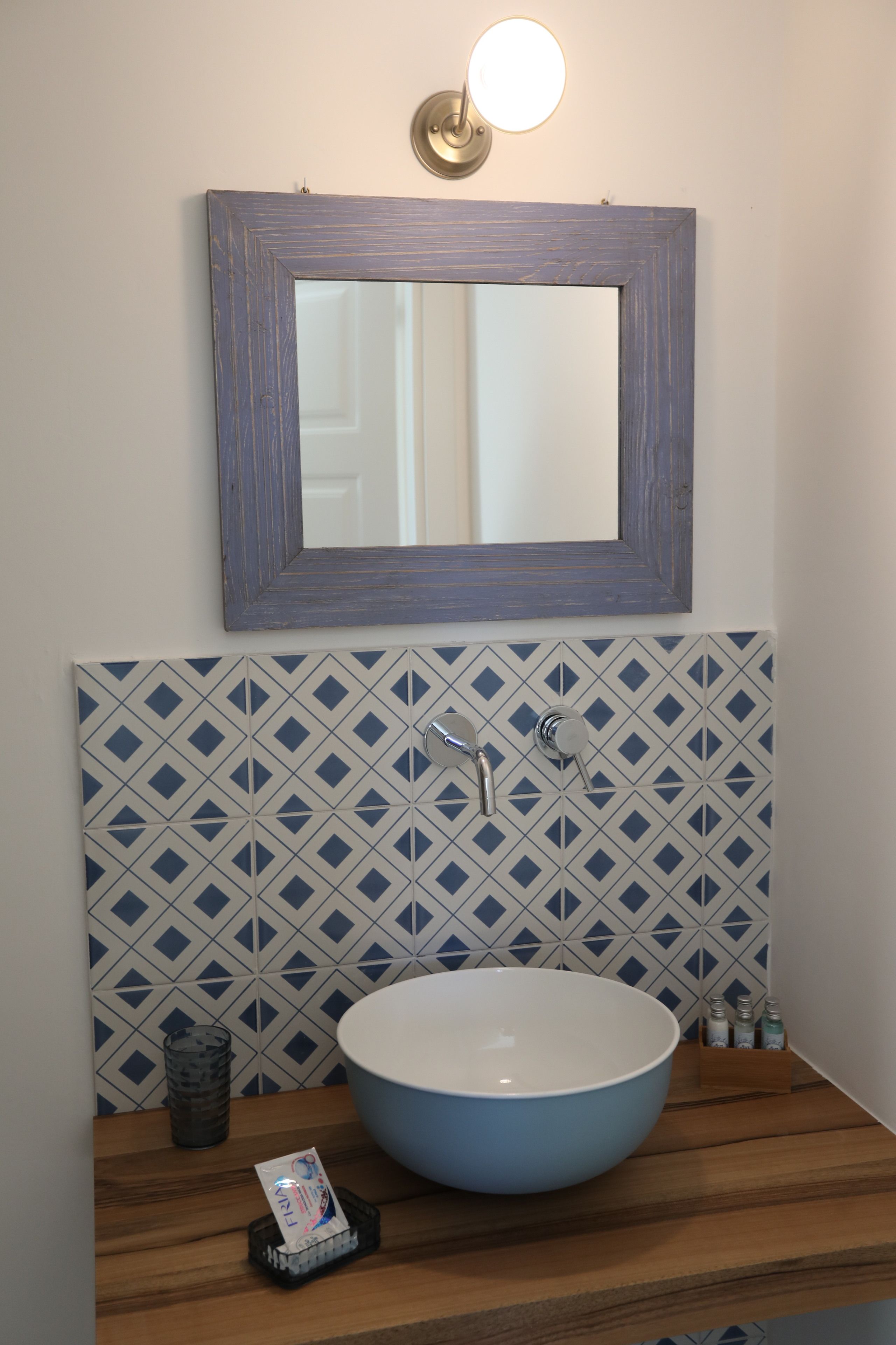 Un baño con un lavamanos azul, un espejo y un salpicadero de azulejos estampados.