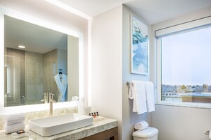 A modern bathroom with a large mirror, a sink, and a toilet. There is a window providing a view of the outside.