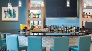 A bar area with teal chairs, a counter with various bottles, and a large screen. - Best Western Premier Hotel at Fisher's Landing (Vancouver)