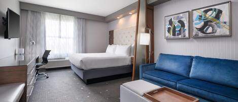 Una habitación de hotel con una cama, un sofá azul, un escritorio con una silla, un televisor y obras de arte en la pared.