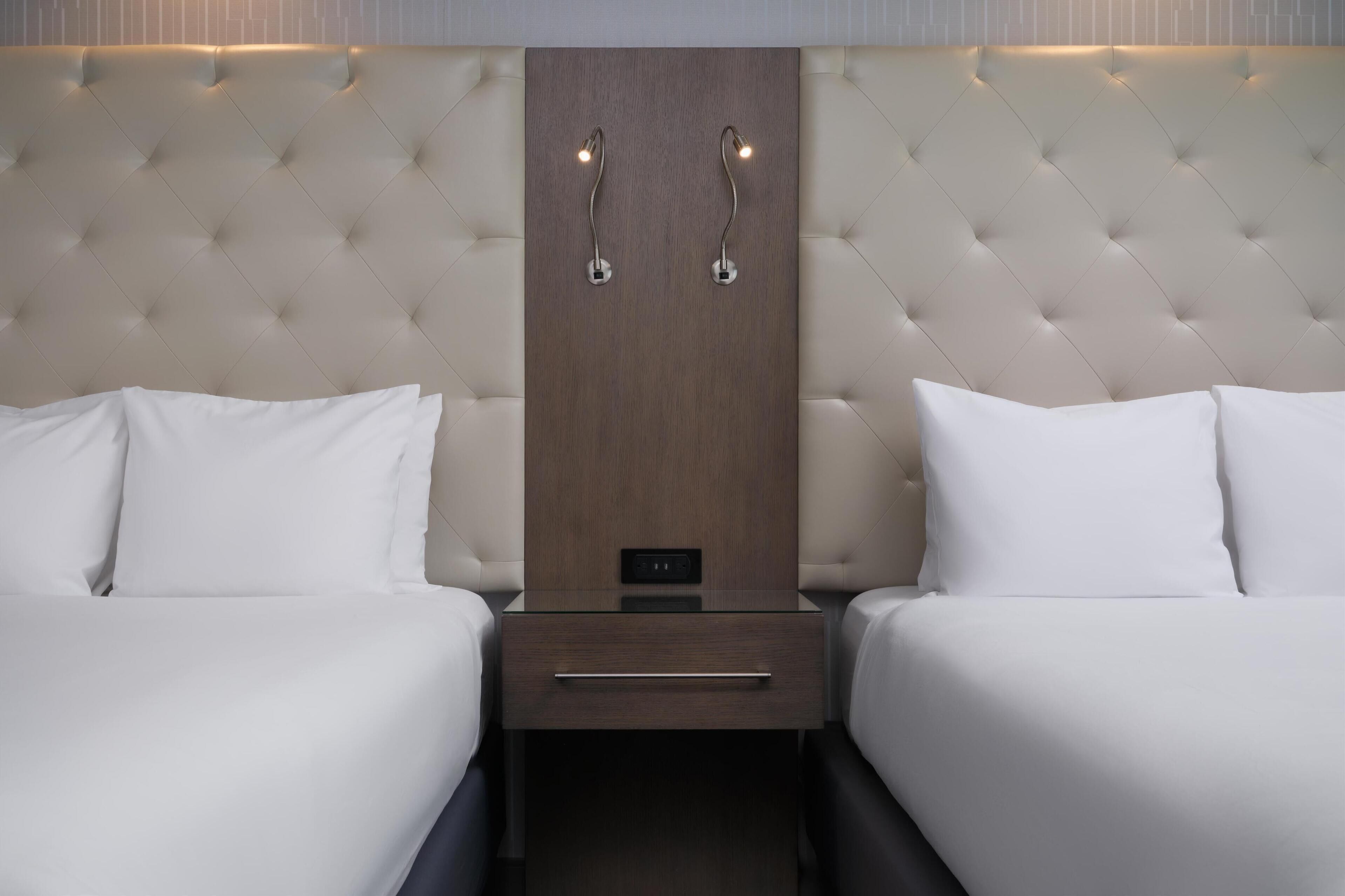 A hotel room with two beds, a wooden headboard, and bedside lamps.