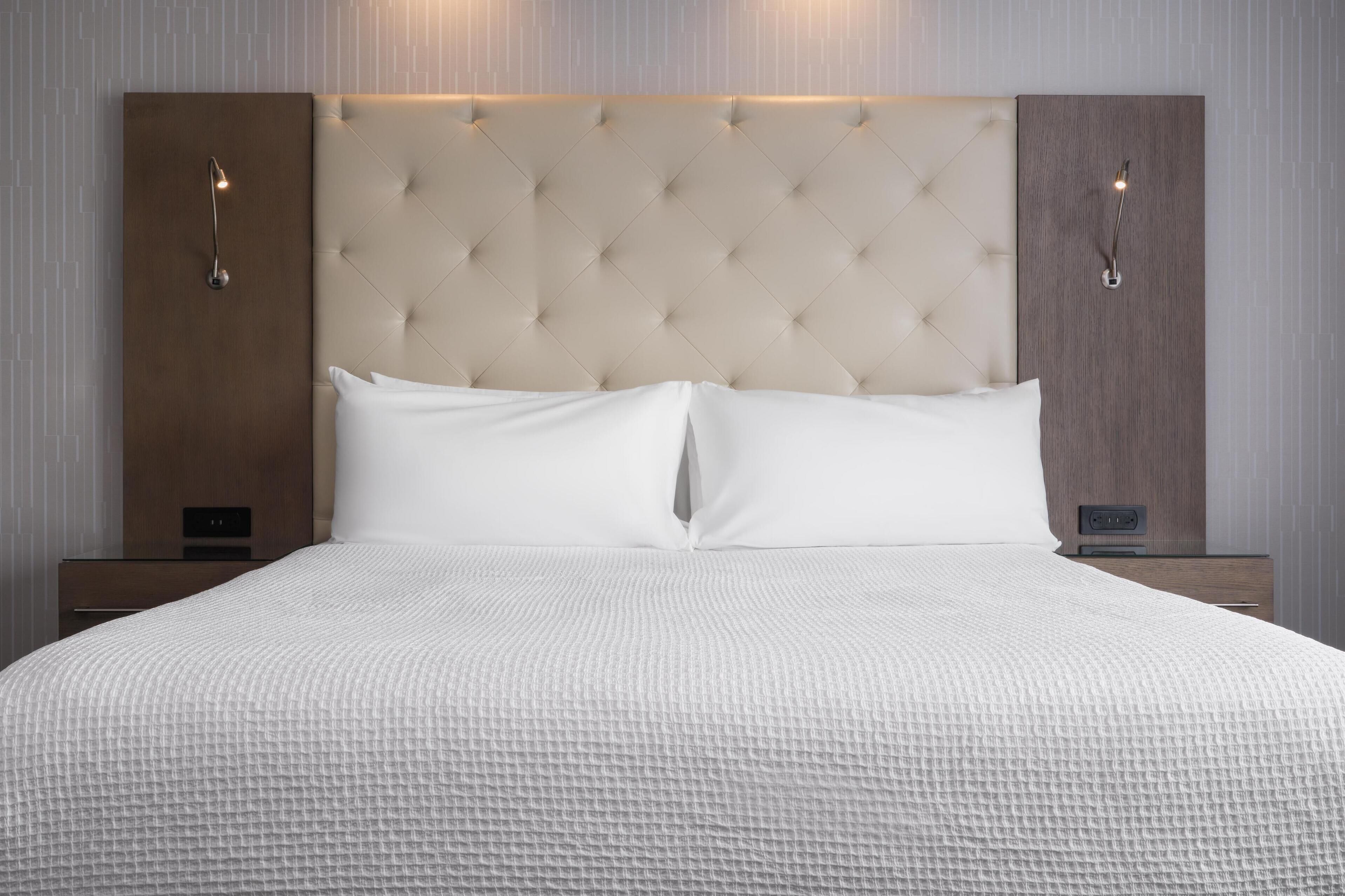 A neatly made bed with a tufted headboard, two bedside tables, and wall-mounted light fixtures.