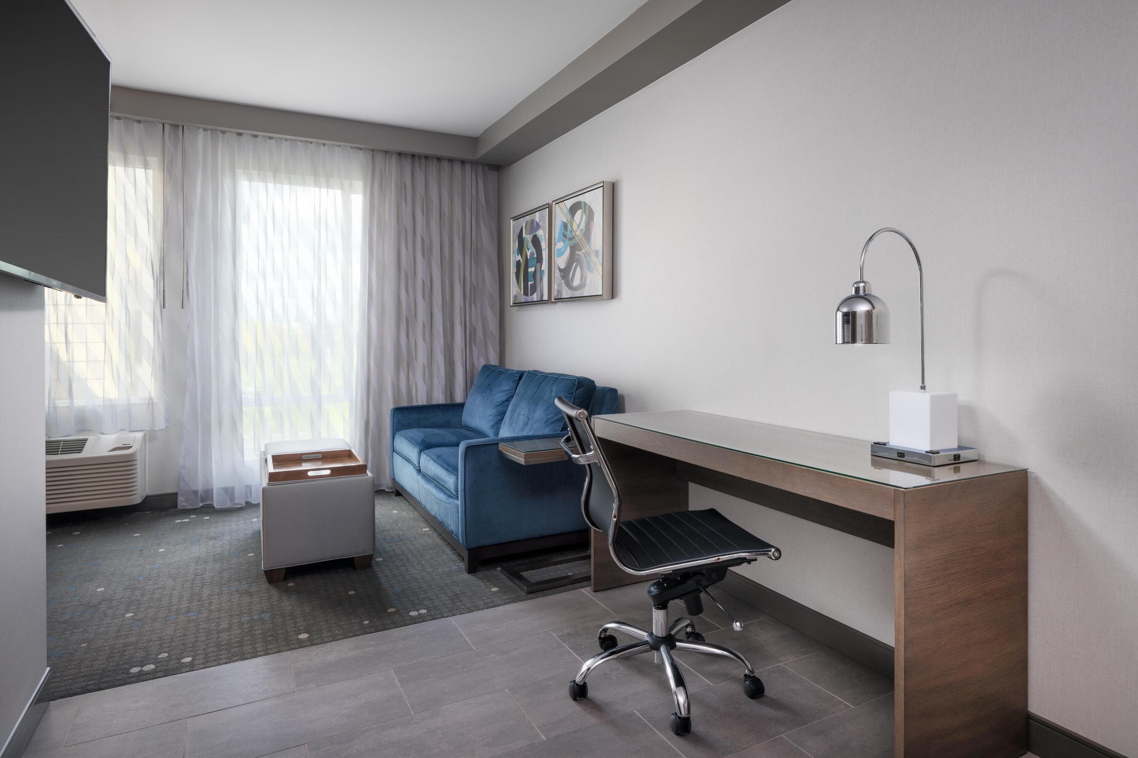 Quarto de hotel moderno com escrivaninha, cadeira e sofá azul.